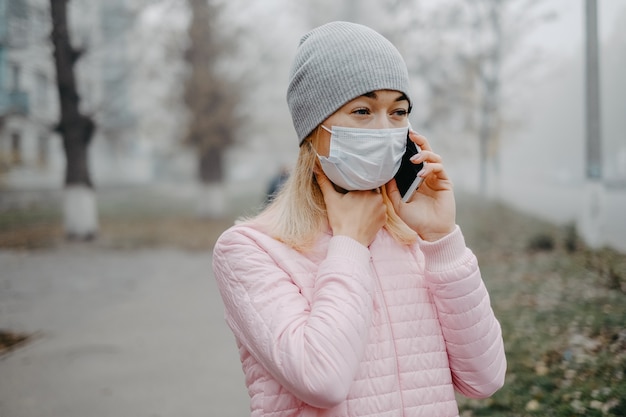 Uma jovem está de pé perto da estrada com uma máscara médica. Proteção contra uma epidemia de vírus em uma cidade no inverno.