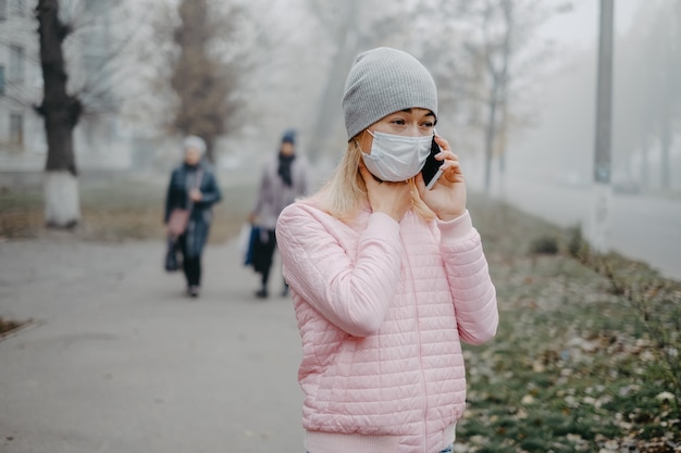 Uma jovem está de pé perto da estrada com uma máscara médica. Proteção contra uma epidemia de vírus em uma cidade no inverno.