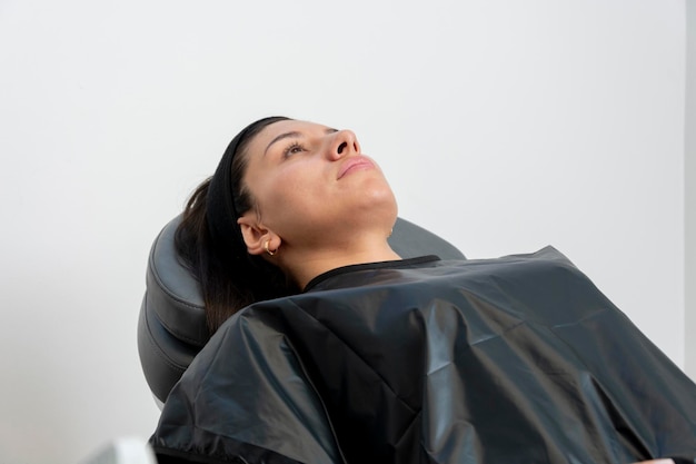 Uma jovem está deitada em uma cadeira de escritório à espera de um tratamento de beleza em seus lábios