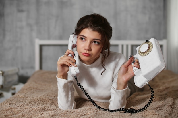 Foto uma jovem está deitada em uma cama e fala ao telefone em casa