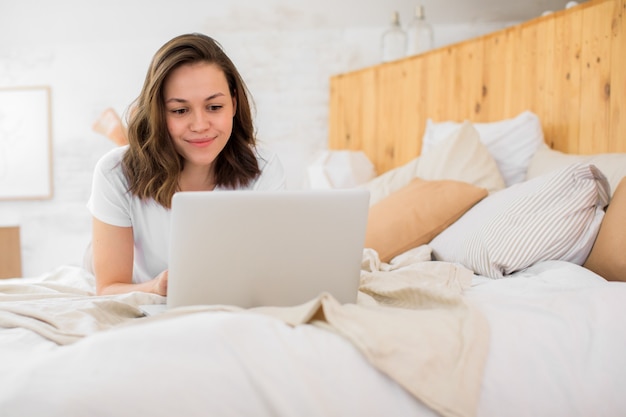 Uma jovem está deitada na cama e usa um laptop para videoconferências ou bate-papo com amigos