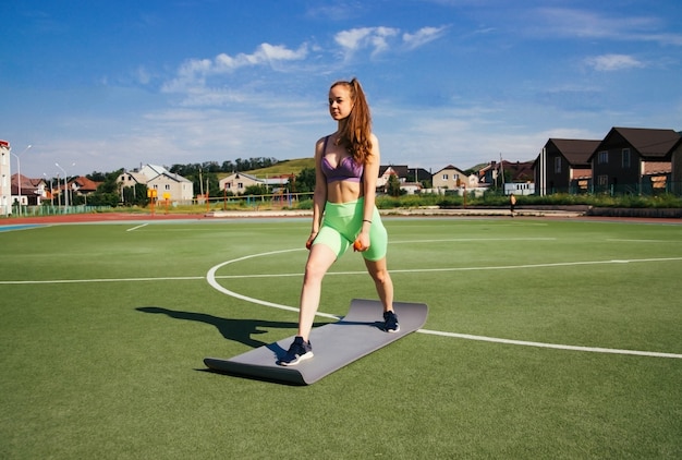 Uma jovem está envolvida em fitness no campo de futebol. Céu azul e sol forte, Um estilo de vida saudável.