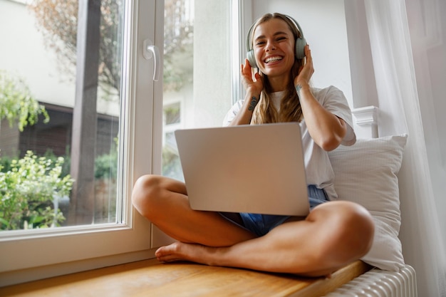 Uma jovem está gostando de ouvir música enquanto trabalha em seu laptop em casa confortavelmente