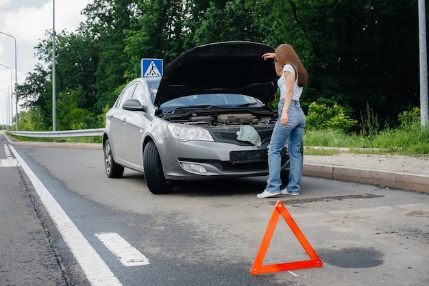 Foto uma jovem está perto de um carro quebrado no meio da rodovia e olha sob o capô. avaria e avaria do carro. esperando por ajuda.