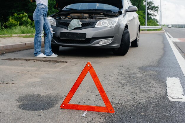 Uma jovem está perto de um carro quebrado no meio da rodovia e olha sob o capô. Avaria e avaria do carro. Esperando por ajuda.