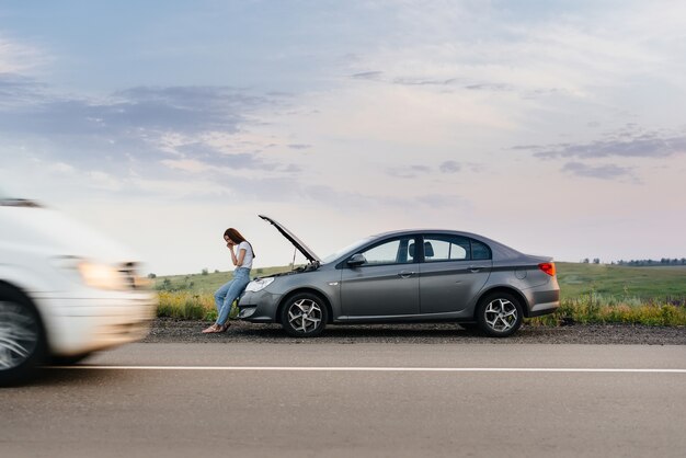 Uma jovem está perto de um carro quebrado.