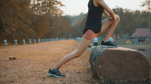 Uma jovem está se aquecendo antes de correr na natureza ao ar livre ao pôr do sol.