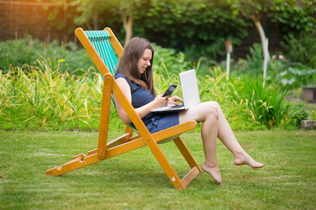 uma jovem está sentada em um prado com um laptop e falando em uma conferência online no trabalho