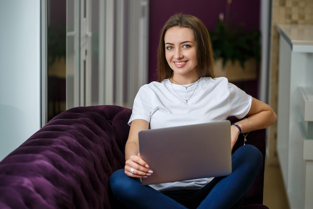 Uma jovem está sentada no sofá e trabalhando em um laptop remotamente do trabalho