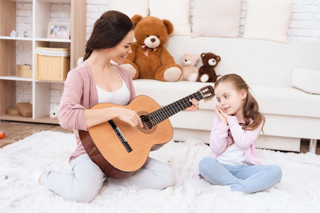 Uma jovem está tocando violão e uma garota está cantando.