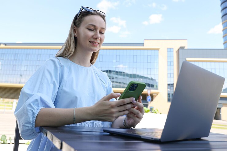 Foto uma jovem está trabalhando em um laptop e segurando um telefone em um terraço de verão