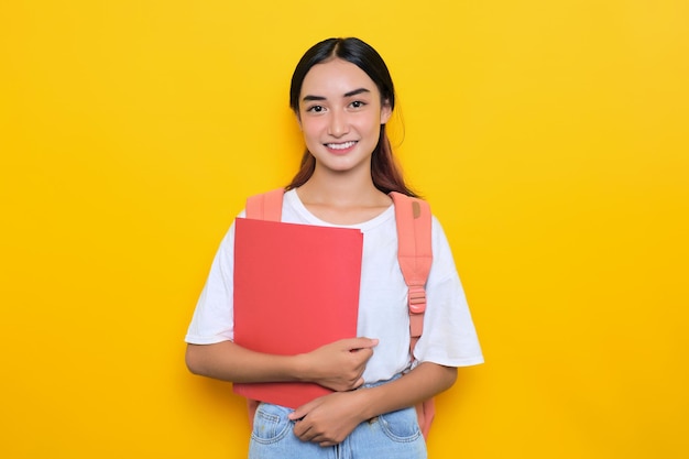 Uma jovem estudante alegre usando mochila segurando livros isolados em fundo amarelo