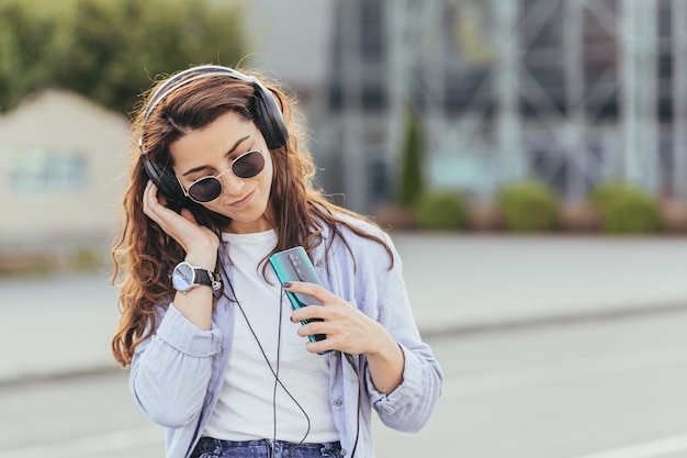 Uma jovem estudante bonita esperando um carro de táxi e ouvindo música