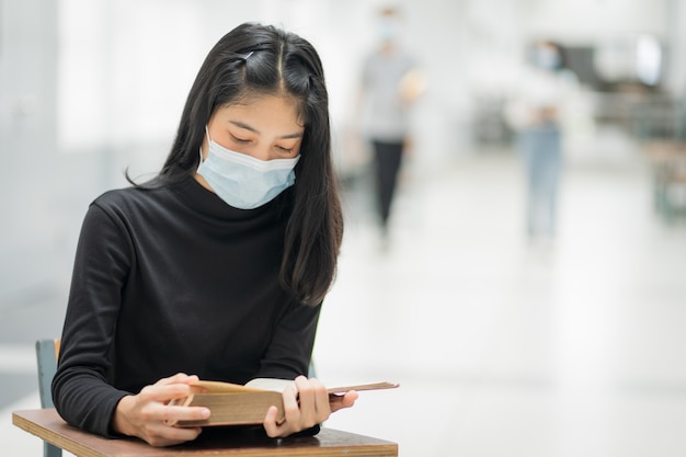 Uma jovem estudante universitária asiática usa uma máscara médica com uma mochila escolar para se proteger da pandemia do vírus da gripe COVID-19 enquanto estudava no campus da faculdade. Foto de estoque de educação