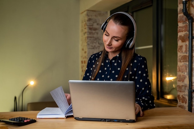 Foto uma jovem estudante universitária estuda online usando um laptop uma garota sorridente está assistindo a um webinar ou educação virtual escrevendo em um caderno