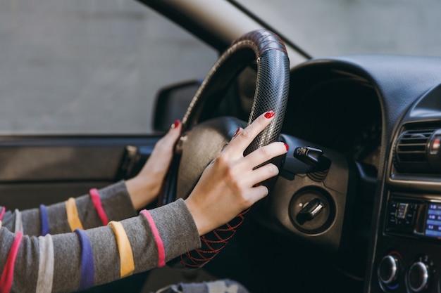 Uma jovem europeia com pele limpa e saudável colocou as mãos com manicure vermelha nas unhas no volante do carro com interior preto. viajar e dirigir o conceito.