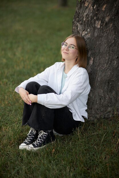 Uma jovem europeia de óculos está descansando em um parque em uma aduela verde. Retrato de uma garota