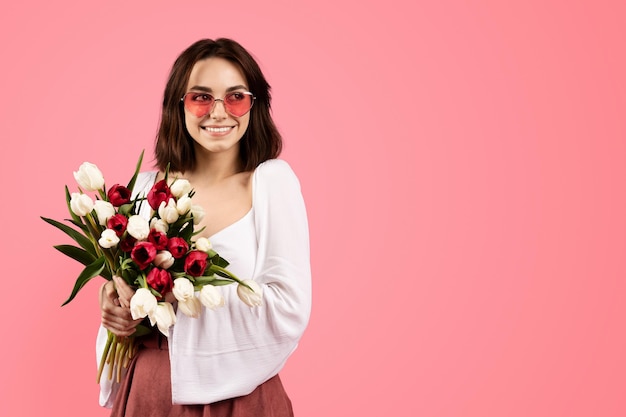 Uma jovem europeia sorridente em copos com buquê de flores desfruta do estilo de vida e se regozija nas férias de primavera