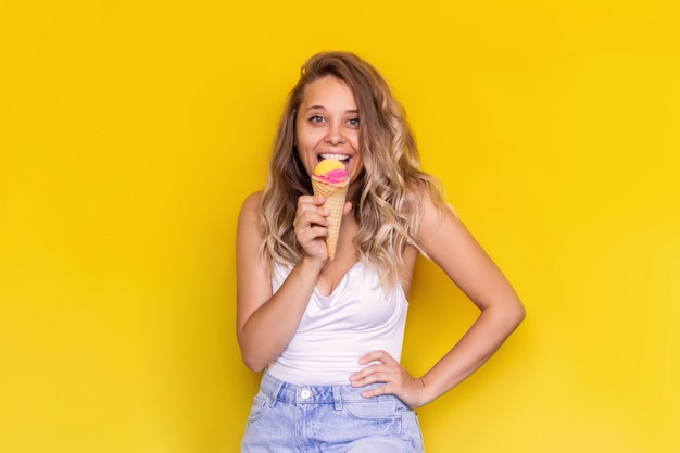 Uma jovem excitada come sorvete de sorvete de frutas em uma casquinha de waffle em um fundo de cor amarela