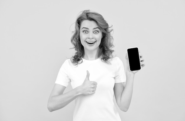 Uma jovem excitada isolou o fundo amarelo usando o celular mostrando o gesto okey