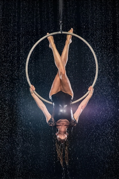 Foto uma jovem executa os elementos acrobáticos no anel aéreo. apresentações de tiro do aqua studio em um fundo preto.