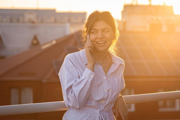 Uma jovem falando ao telefone na varanda ao pôr do sol