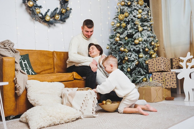 Uma jovem família alegre com uma criança pequena descansa perto da árvore de Natal em casa Casa de casal com decoração de Natal em casa Natal tempo de Ano Novo para celebrar