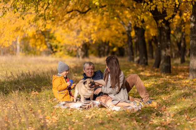 Uma jovem família com uma criança pequena e um cachorro passam um tempo juntos para um passeio no parque de outono