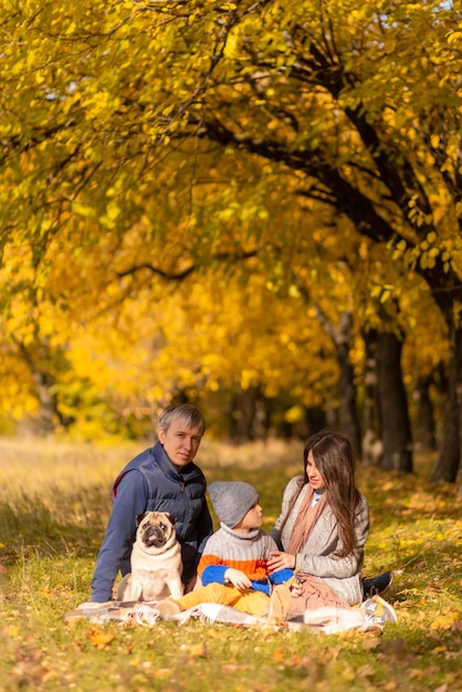 Uma jovem família com uma criança pequena e um cachorro passam um tempo juntos para um passeio no parque de outono