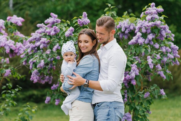 Uma jovem família feliz com um bebé está a relaxar no parque de lilas em flor da primavera.