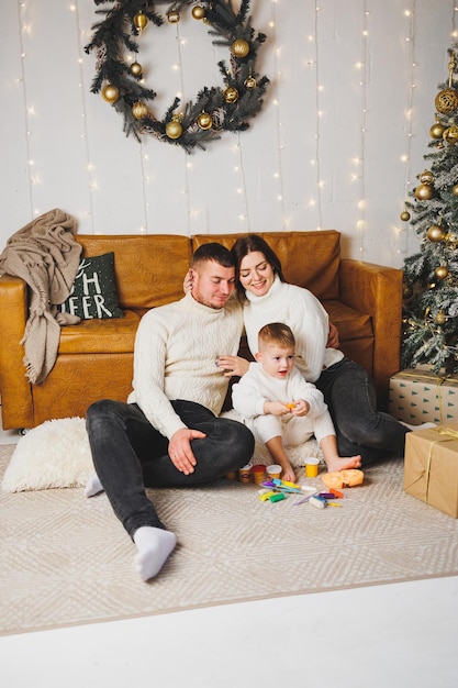 Uma jovem família feliz com uma criança pequena está comemorando o Ano Novo em casa perto da árvore de Natal Natal com a família na época do Ano Novo para comemorar