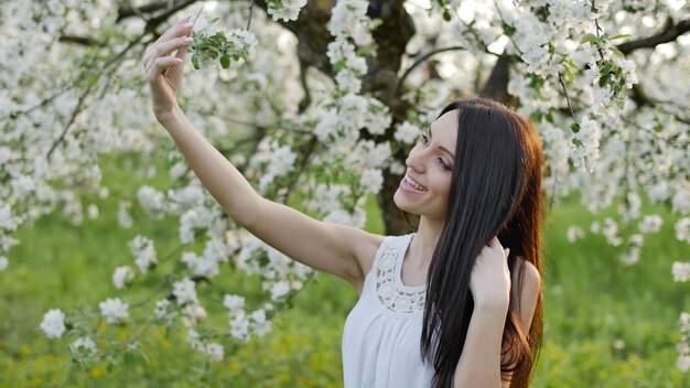 Uma jovem faz selfie em um pomar de maçãs, na primavera.