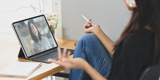 Foto uma jovem fazendo videoconferência com colegas na mesa de trabalho de madeira