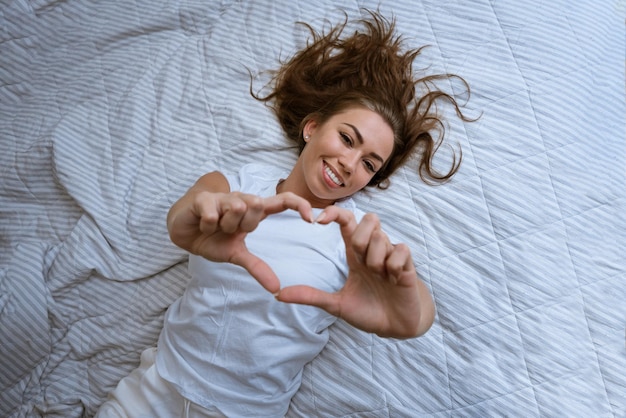 Uma jovem feliz acorda numa cama branca confortável.