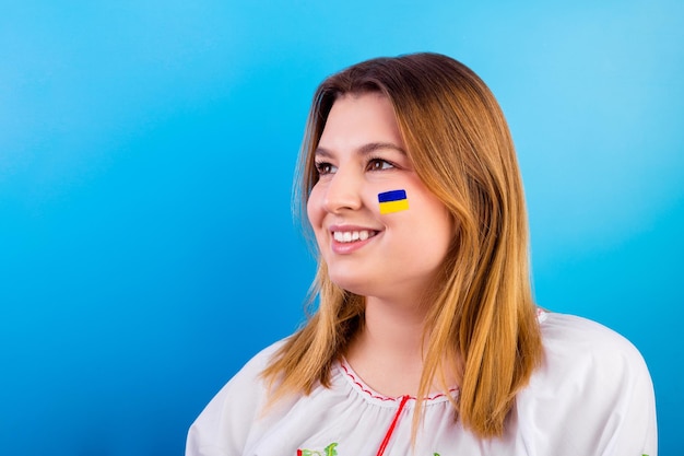 Uma jovem feliz com a bandeira ucrânia no rosto em uma camisa bordada parece um futuro brilhante