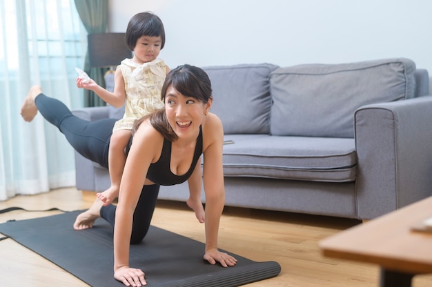 Uma jovem feliz em roupas esportivas com a filha se exercitando na sala de estar em casa