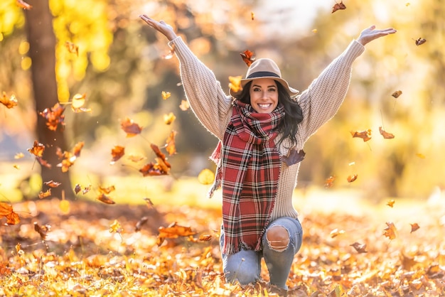 Uma jovem feliz em um parque joga folhas durante um verão indiano e gosta de outono