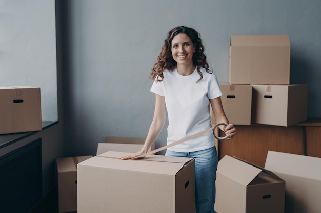 Uma jovem feliz está embalando caixas com fita adesiva Trabalhador de serviço em movimento preparando carga