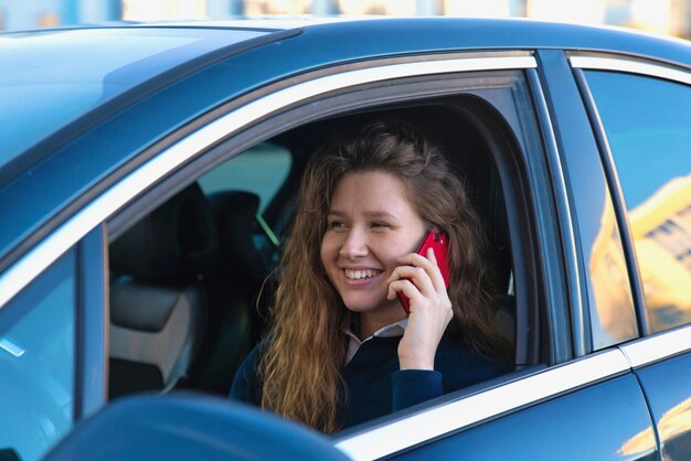 Uma jovem feliz está sentada em seu automóvel, gostando de dirigir Uma senhora alegre em um automóvel, falando no celular, ligando para um smartphone Situação perigosa, motorista descuidado