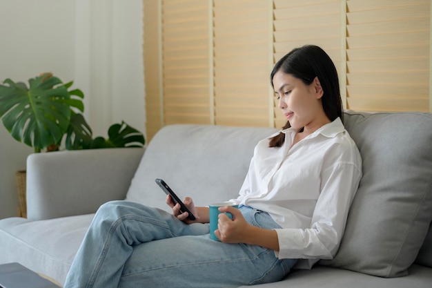 Uma jovem feliz relaxando e usando telefone inteligente em casa, mídia social e conceito de tecnologia