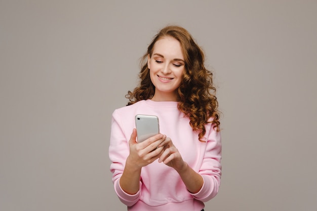 Uma jovem feliz segurando um telefone olha para ele e sorri