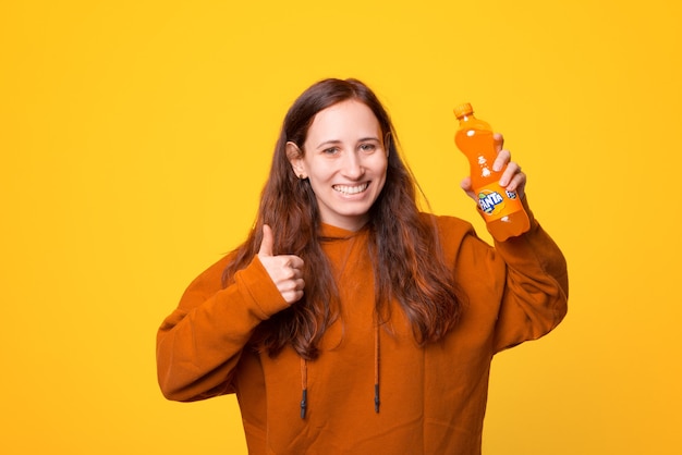 Uma jovem feliz segurando uma garrafa de Fanta e sorrindo com o polegar