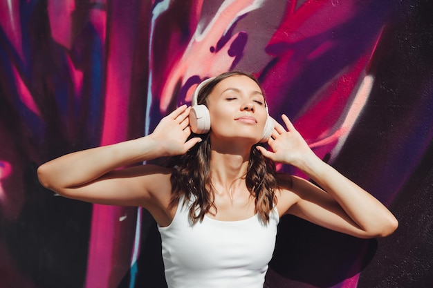 Uma jovem feliz vestida com um top branco e fones de ouvido de saia roxa ouvindo música dançando