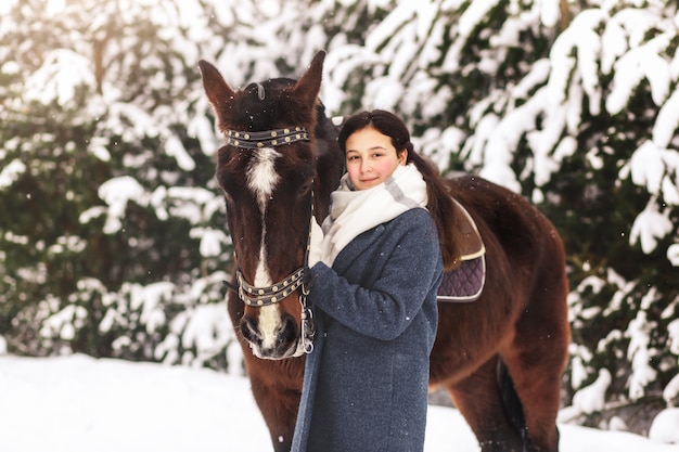 Uma jovem fica ao lado de um cavalo no inverno ao ar livre