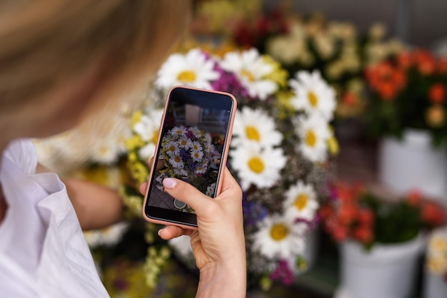 Uma jovem florista está tirando uma foto de um buquê de flores silvestres para uma cliente em sua pequena floricultura