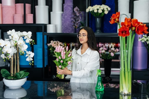 Uma jovem florista feminina cuida de flores em uma floricultura aconchegante e coleta buquês Floricultura e fabricação de baldes em uma floricultura Pequena empresa