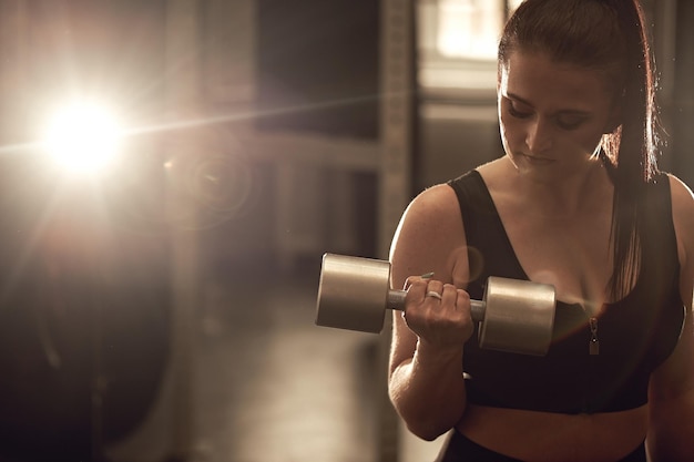 Uma jovem forte e sincera está treinando com halteres na academia Real wokout