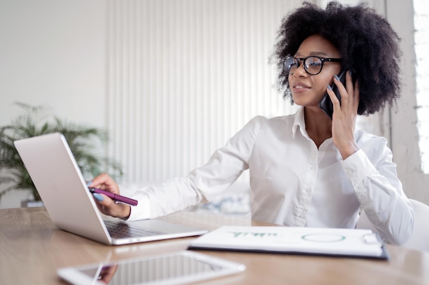 Uma jovem freelance está trabalhando em um escritório em um laptop e falando ao telefone Um local de trabalho