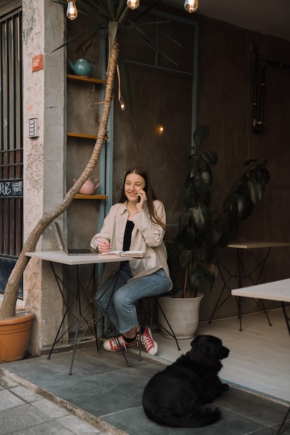 Uma jovem freelancer europeia com longos cabelos escuros em uma camisa e jeans trabalha remotamente em um café