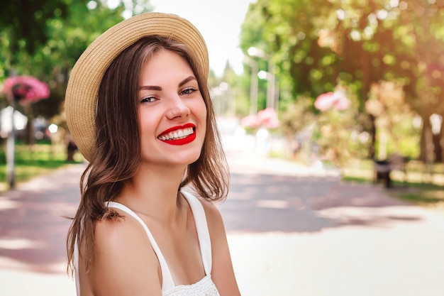 Uma jovem garota caminha no parque e sorri. Retrato, jovem, mulher, chapéu palha, batom vermelho